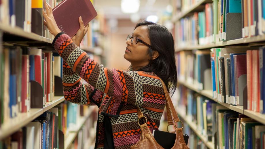 Photograph of student pulling book from library shelves