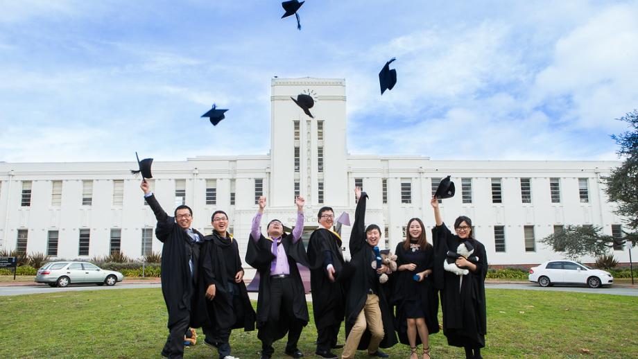 photograph of ANU graduates throwing their caps in front of the School of Art and Design building