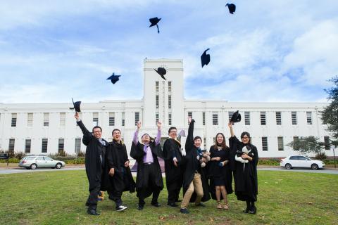 photograph of ANU graduates throwing their caps in front of the School of Art and Design building